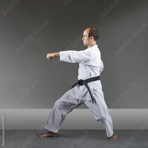 Adult man is training formal karate exercises on a gray background