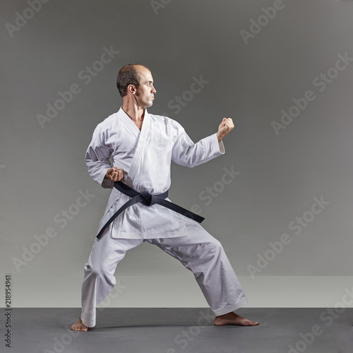 A man in karategi trains formal karate exercises on a gray background