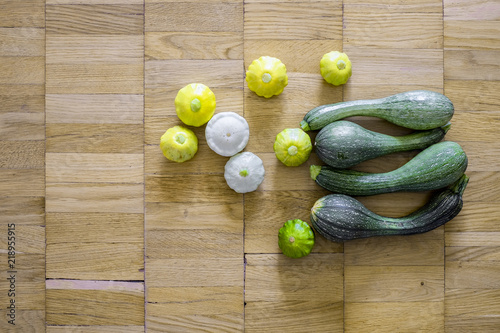 Four green zucchini with small scallop squashes over the light brown wooden background