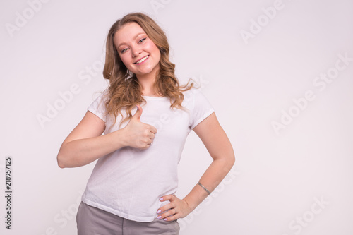 Happy young woman with blond curly hair showing thumb up on white background with copy space