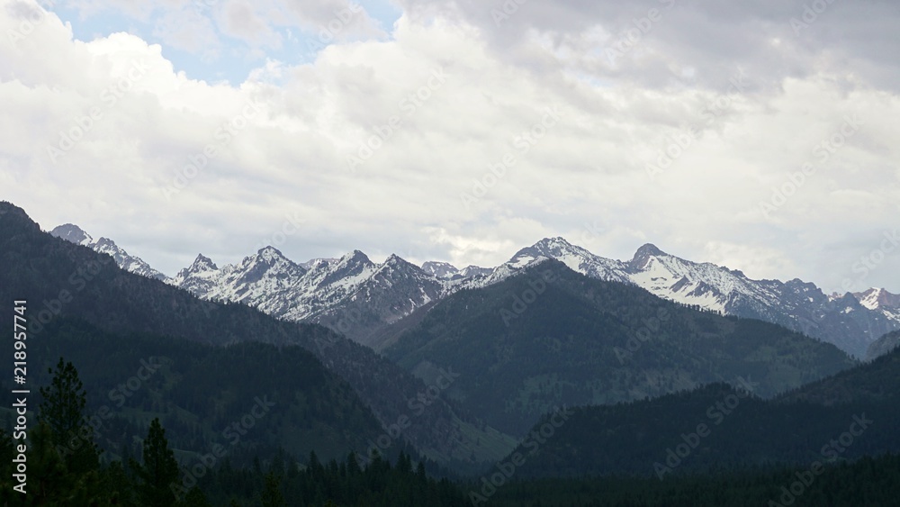 Layers of snow-covered mountain peaks leading off into the distance with stormy clouds overhead