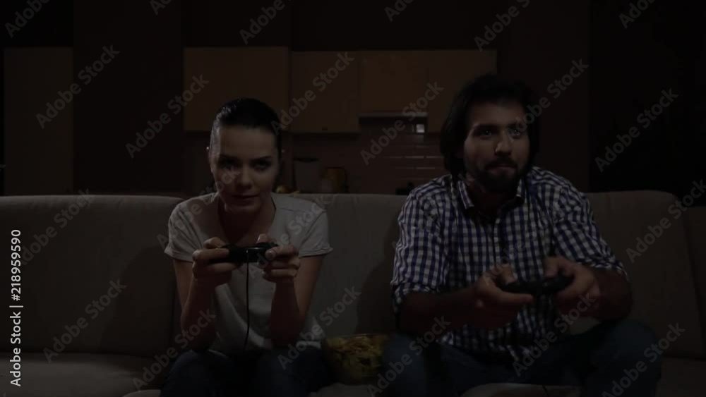Nice view of couple playing gme together. They hold joystick and use it. They try to play as best as possible. Game is intense. They sit on sofa. Nice view of couple playing gme together. They hold joystick and use it. They try to play as best as possible. Game is intense. They sit on sofa.
