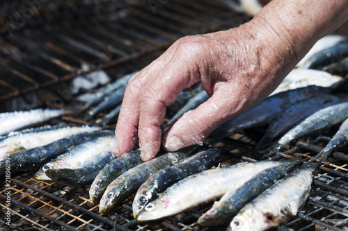 old woman salting some sardines in a grill