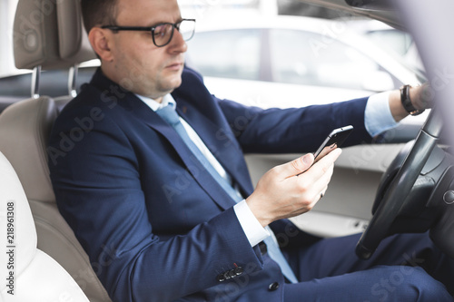 a businessman driving a prestigious car holds a mobile phone in his hand. Hasty life