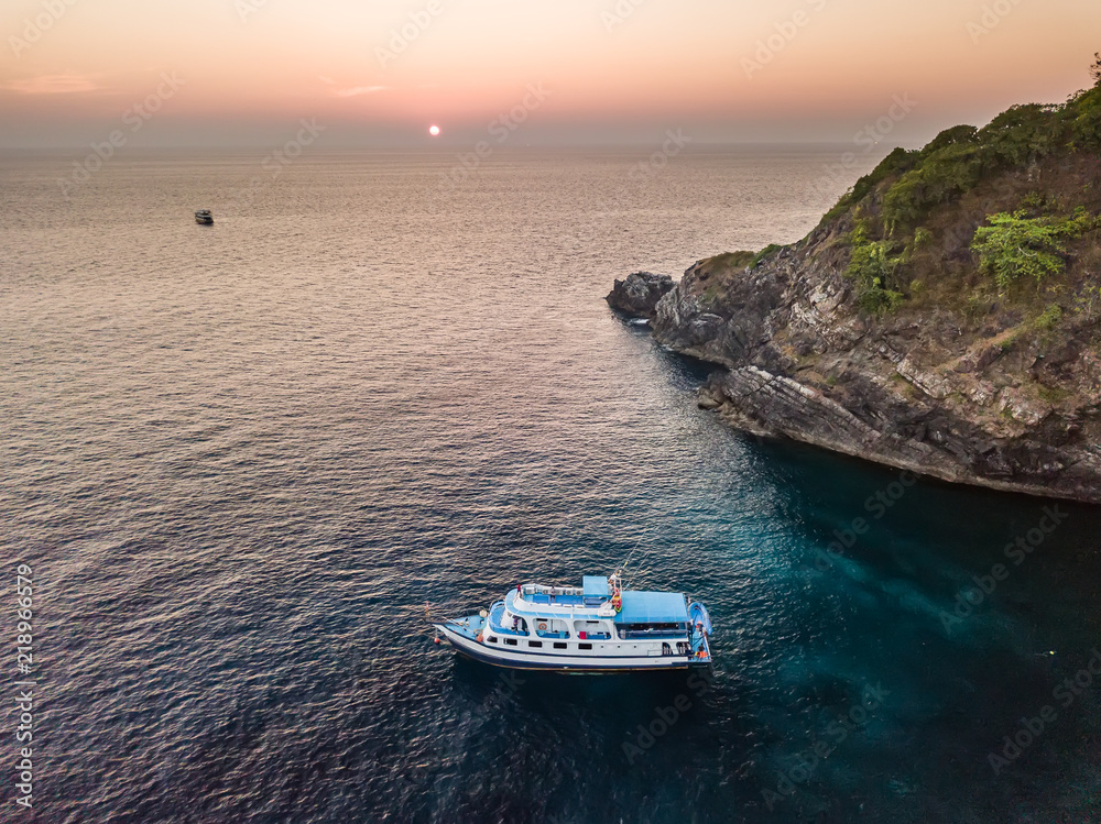 Aerial drone view of a tropical sunset next to a remote island with a single boat at anchor (Koh Bon)