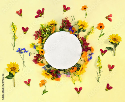 Fototapeta Naklejka Na Ścianę i Meble -  Creative decoration summer flowers sunflowers, calendula, linaria, daisies, red samaras maple ash, cornflowers with circle card note with space for text on yellow paper background. Top view, flat lay