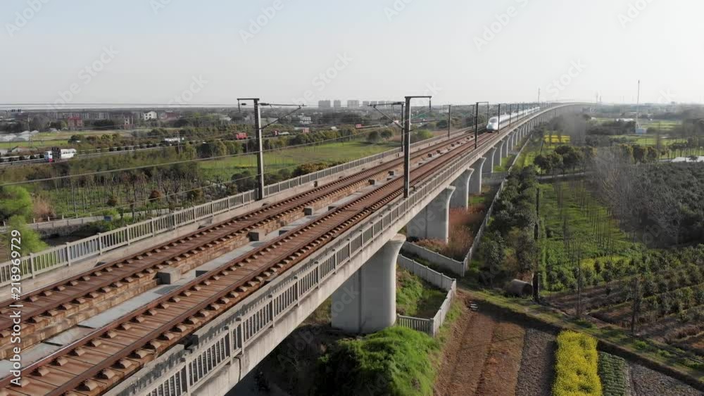 Aerial of raised railway of Chinese high speed rail. China's bullet train CSR zooming through the rural countryside. Drone shot of moving Gao Tie on elevated railway.