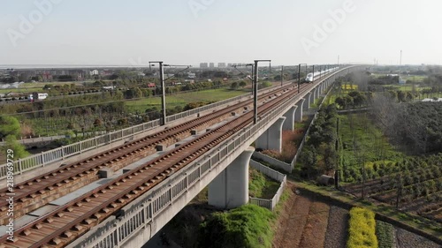 Aerial of raised railway of Chinese high speed rail. China's bullet train CSR zooming through the rural countryside. Drone shot of moving Gao Tie on elevated railway.