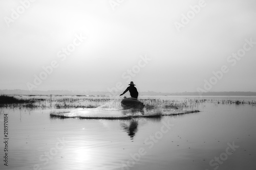 Silhouette of fishermen casting for catching the fish on the wooden boat at the lake in the morning © Shinonome Studio