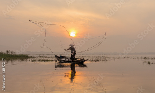 Silhouette of fishermen casting for catching the fish on the wooden boat at the lake in the morning