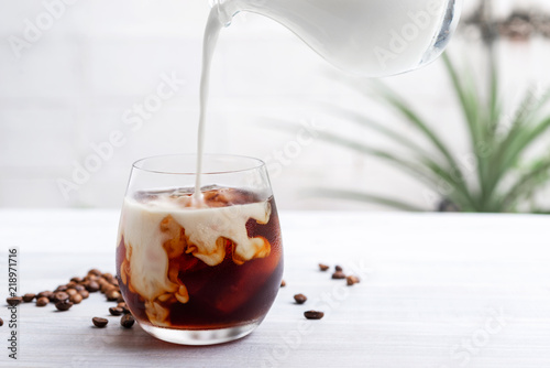 Pouring milk into a glass of homemade cold brew coffee on wooden table Fototapet