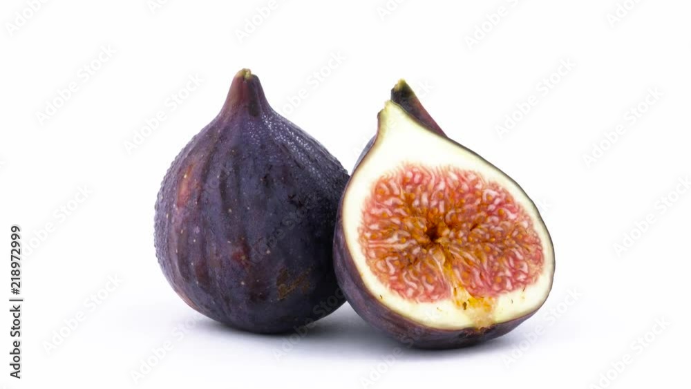 One whole and two halves of mature common fig fruit with water drops. Slowly rotating on the turntable isolated on the white background. Close-up. Macro. One whole and two halves of mature common fig fruit with water drops. Slowly rotating on the turntable isolated on the white background. Close-up. Macro.