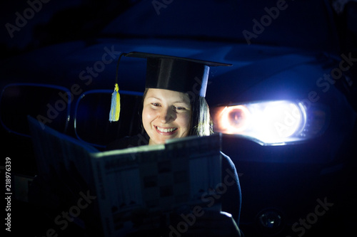 Young woman with student suit sitting near by SUV car headlamp, smilling