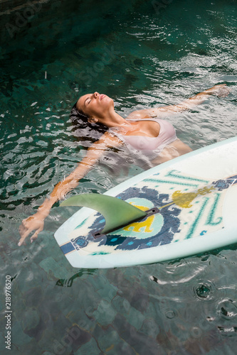 Photography Beautiful young woman in sexy bikini relax in pool with her longboard single fin surfing board under tropical rain