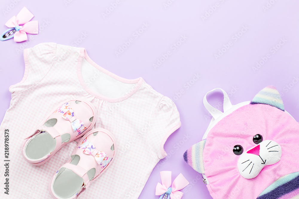 Little girl clothes collection flat lay with t-shirt, jeans, sandals, backpack on pastel background.