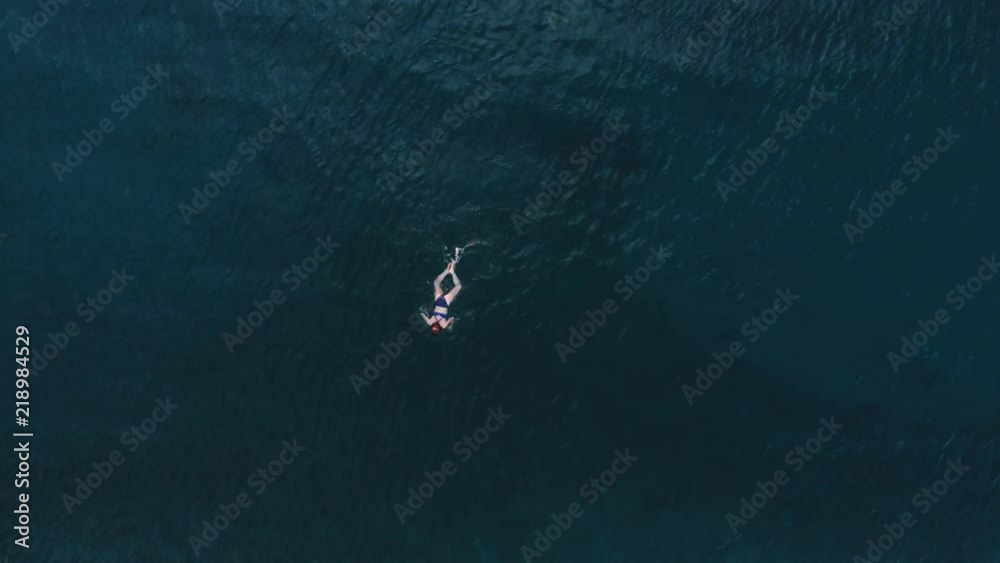 AERIAL: woman floating on blue water surface, swimming in transparent mediterranean sea, top down view, summer vacation concept. AERIAL: woman floating on blue water surface, swimming in transparent mediterranean sea, top down view, summer vacation concept.