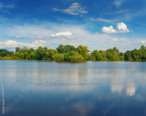 Tranquil landscape at a lake  with the vibrant sky  white clouds and the trees reflected