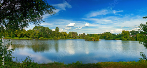 Tranquil landscape at a lake, with white clouds sky and the trees reflected i...