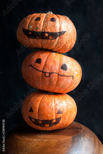 Halloween pumpkins with funny faces. Column of three pumpkins. Dark background.