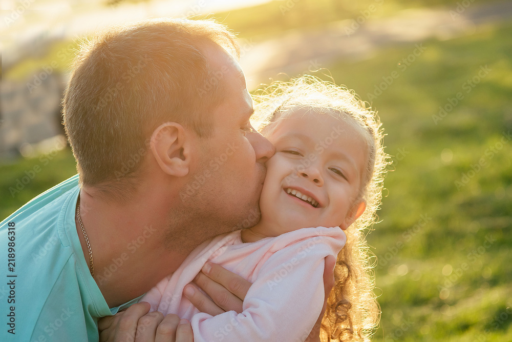 close-up portrait of father kissing happy little girl on cheek in summer park close-up portrait of father kissing happy little girl on cheek in summer park