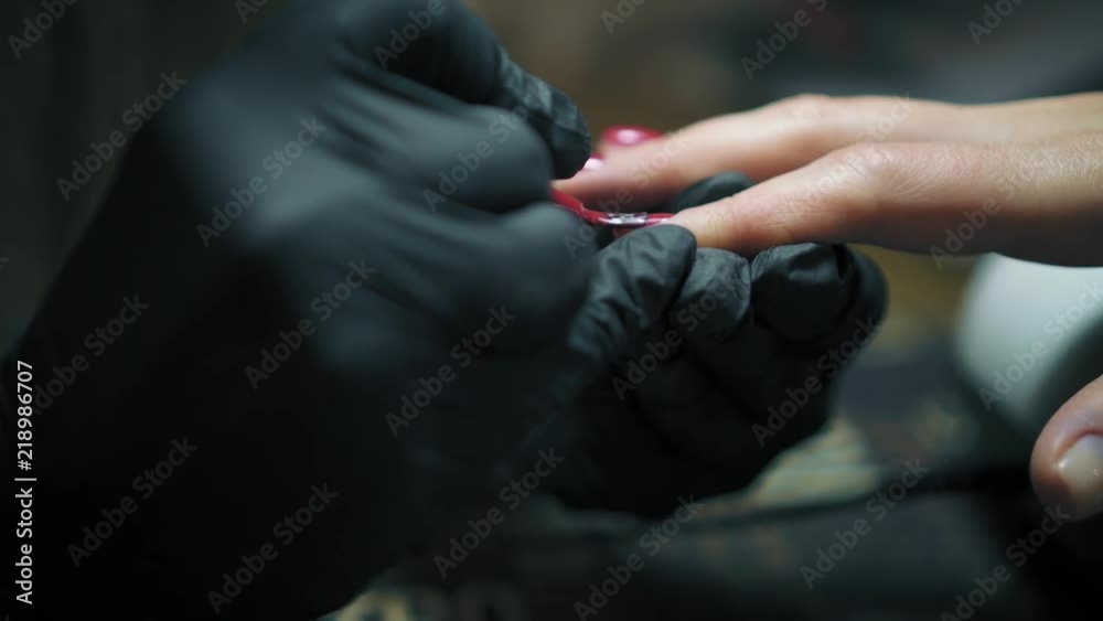 Close up view of professional nail artist in black gloves carefully polishing woman's nails with red nail polish in nail salon. Manicure Close up view of professional nail artist in black gloves carefully polishing woman's nails with red nail polish in nail salon. Manicure