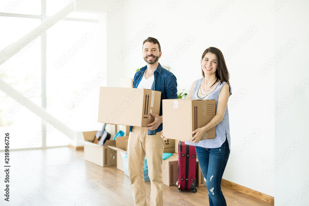Happy Couple Carrying Cardboard Boxes In New Home Happy Couple Carrying Cardboard Boxes In New Home