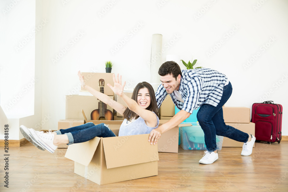 Man Pushing Woman Sitting In Cardboard Box In New Home Man Pushing Woman Sitting In Cardboard Box In New Home