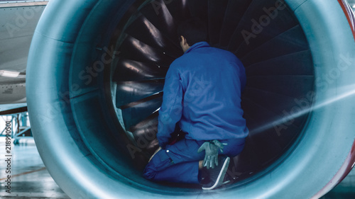 Aircraft maintenance mechanic with a flash light inspects plane turbine blades in a hangar.