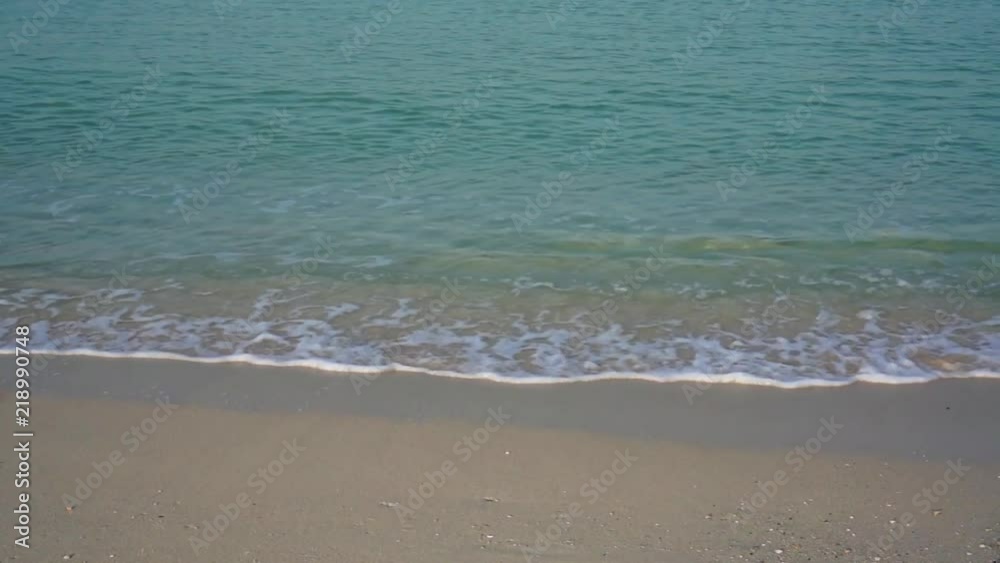Wave of the sea on the sandy beach at the sunrise.