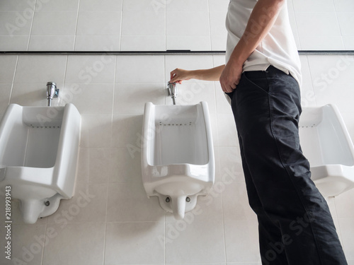 Man standing press flushing a urinal in a public washroom