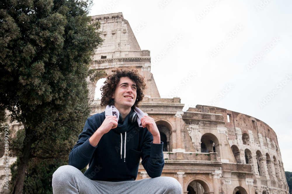 Handsome young sportsman relaxing after training with a towel around his neck in front of Colosseum in Rome