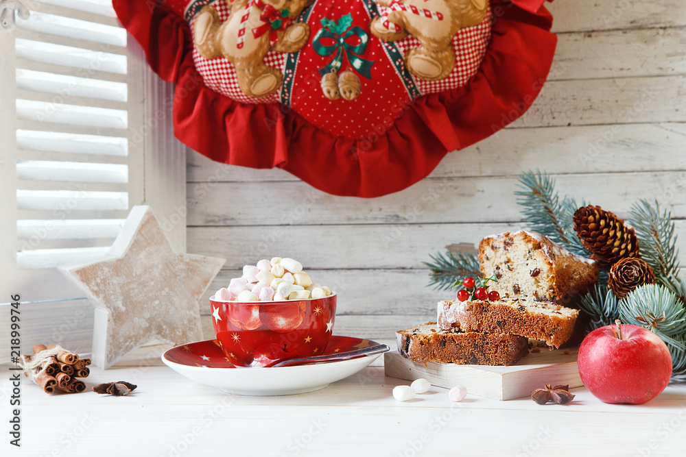 Fototapeta premium Cup of hot drink with marshmallow and Christmas cupcake. Composition with Christmas wreath, fur-tree branches and Christmas decorations. Close up on white vintage window with wooden shutters.