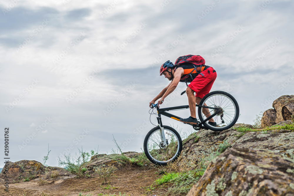 Cyclist in a helmet and with a backpack riding down the rock on a mountain bike, an active lifestyle.