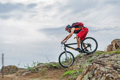 Fototapeta Naklejka Na Ścianę i Meble -  Cyclist in a helmet and with a backpack riding down the rock on a mountain bike, an active lifestyle.