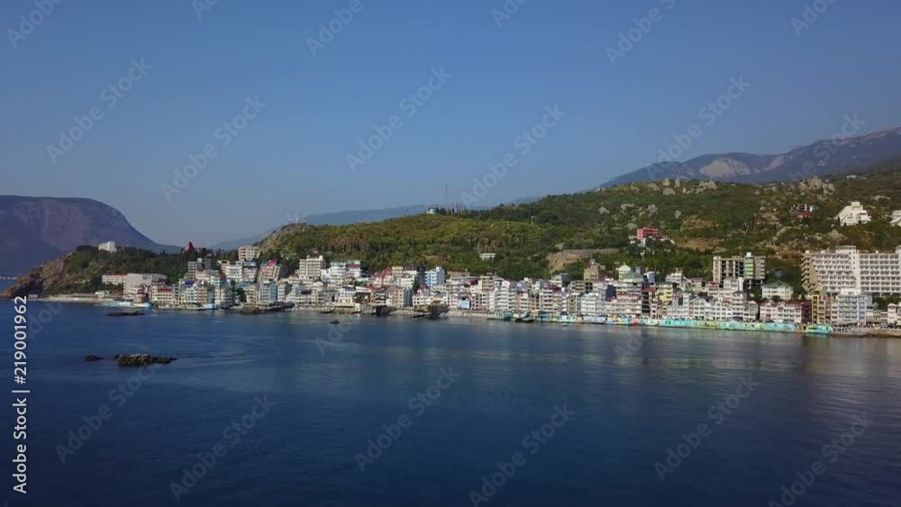 Aerial establishing opening shot of beautiful colorful european cityscape on the mountains over sea. Dense multi-storey building by the shore in the resort. Camera flies forward. Crimea, Utes. Aerial establishing opening shot of beautiful colorful european cityscape on the mountains over sea. Dense multi-storey building by the shore in the resort. Camera flies forward. Crimea, Utes.