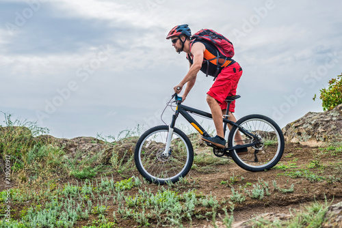 Cyclist riding a mountain bike on rocks on the blue sky background.