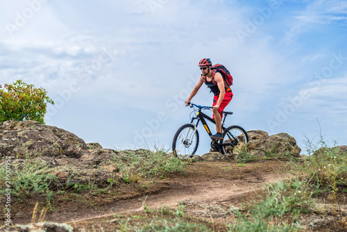 Cyclist riding a mountain bike on rocks on the blue sky background.