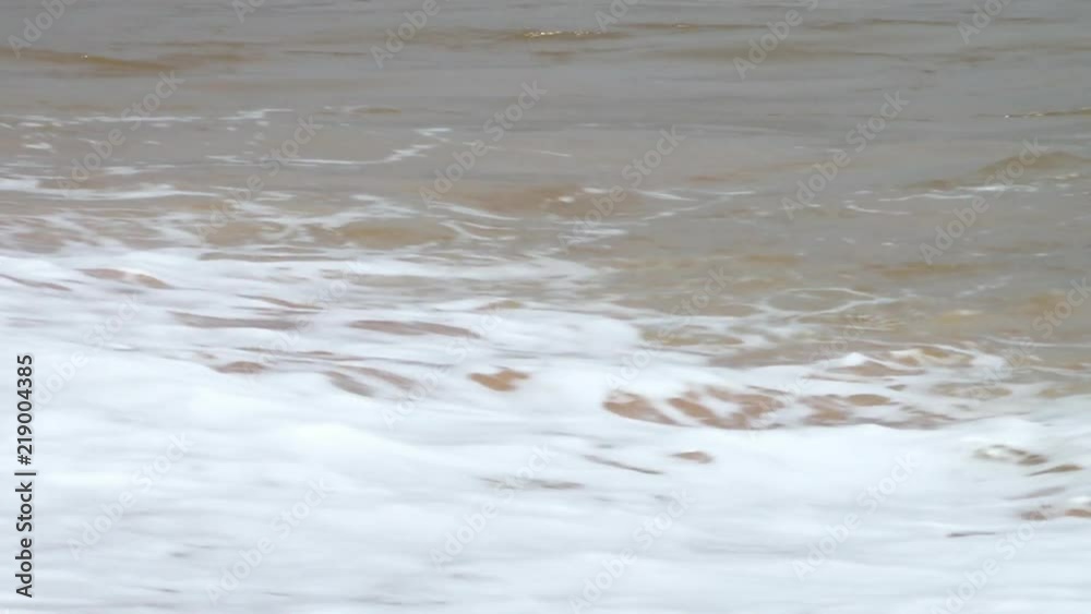 Closeup tracking shot on a beach showcasing waves rolling and crashing up on shore Closeup tracking shot on a beach showcasing waves rolling and crashing up on shore