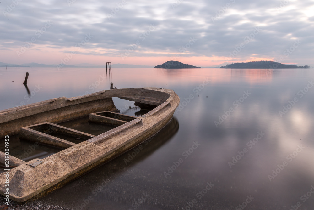 Beautiful view of Trasimeno lake (Umbria) at dusk, with a little, old boat partially filled by water, perfectly still water and a mackerel sky