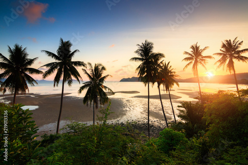 Sunset over the tropical beach with coconut palm and boat at Chumphon , Thailand . silhouettes of palm trees and amazing cloudy sky on sunset at tropical Beach with Lens Flare
