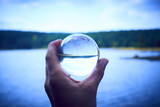 Hand holding a glass ball reflecting the lake and the forest. Concept of environment, nature protection, ecology. Selective focus