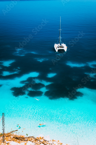 White catamaran yacht drift on clear azure water surface in calm blue lagoon with transparent water and dark pattern on bottom