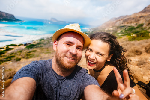 Young happy couple taking selfie photo with island and turquoise water. Self portrait of couples in vacation