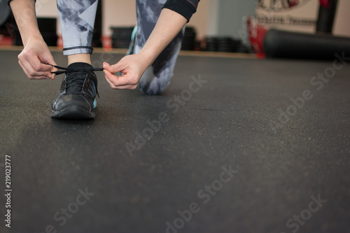 Woman tying her shoe in a gym, preparing for workout or run, wearing gray leggings