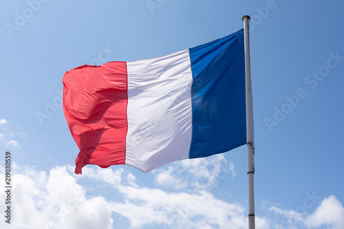 French Tricolour flag blowing in the wind on a blue sky day