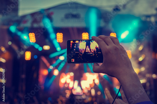 Man holding smartphones in hands and photographing and shoots a video. Taking photo on front stage on summer outdoor music concert festival.