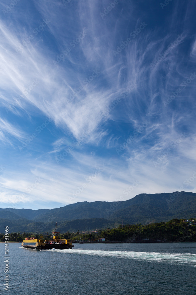 Panoramic view with a ferryboat crossing the sea with mountain and blue sky on sunny summer day in Ilha Bela on the coast of São Paulo, Brazil.