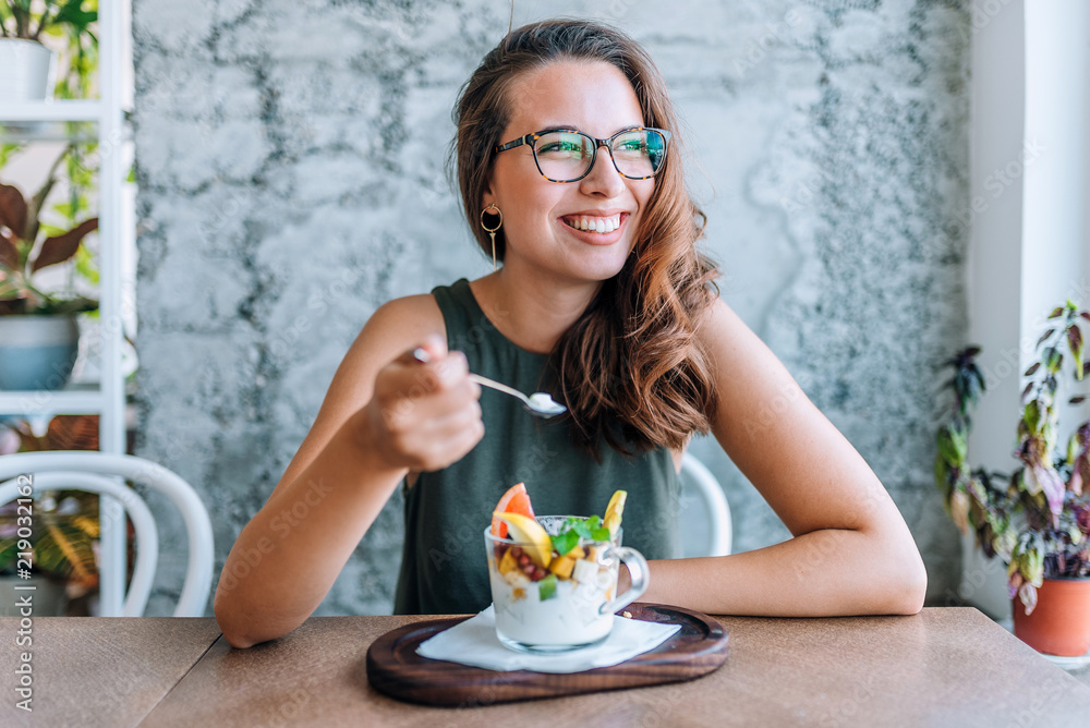 Young cheerful woman eating fruit salad. - obrazy, fototapety, plakaty 