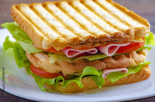 Close up of fresh sandwich with ham, bacon,tomatoes on white plate