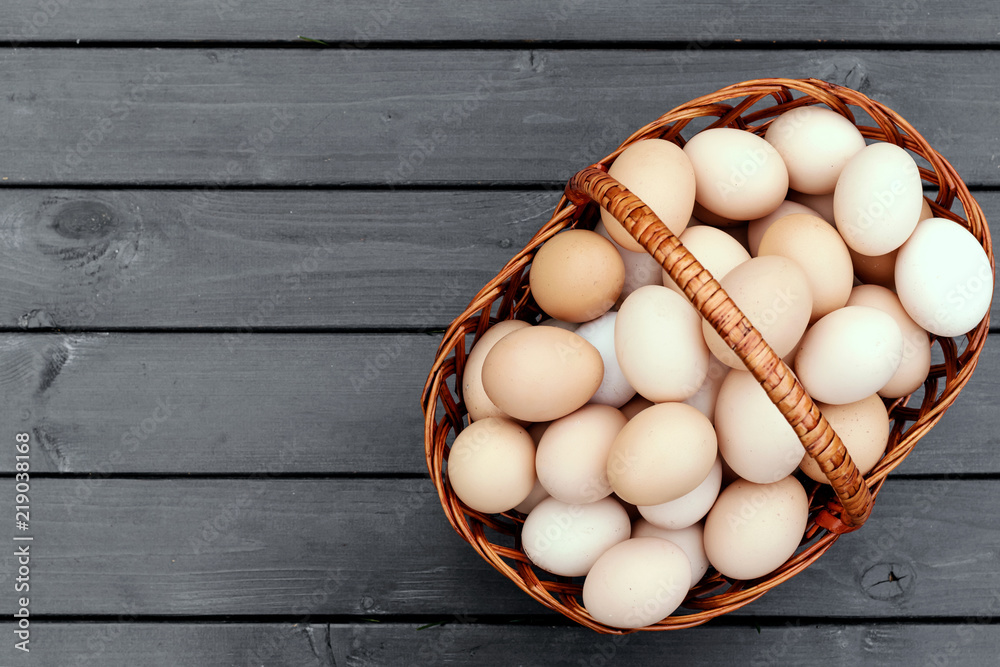 Chicken eggs and quail eggs in basket on black wooden background.